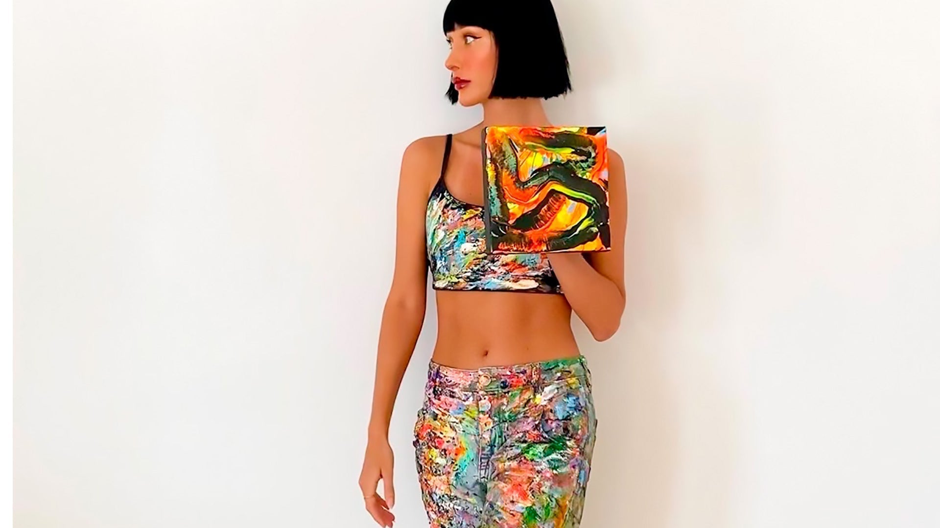 Image of Bridget Bradley, Abstract expressionist Artist, in the early days, wearing her painting clothes holding a small original abstract painting.