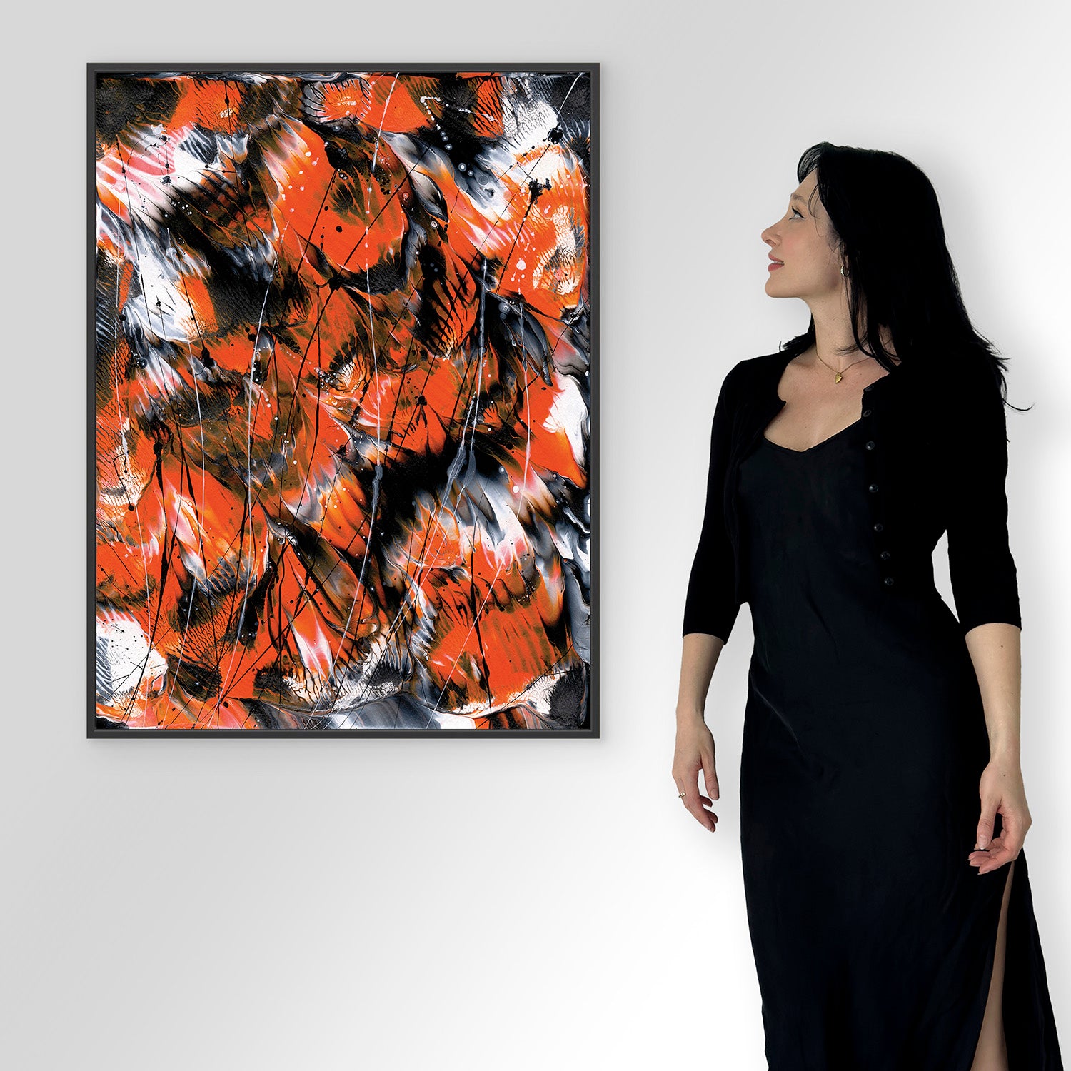 Bridget Bradley in a black outfit standing next to an abstract fine art print with orange, black, and white colours on a white wall.