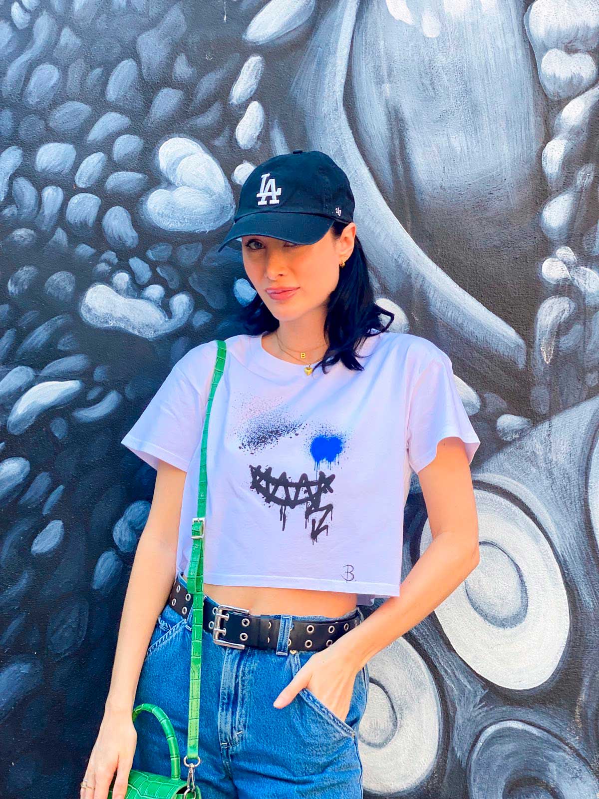 Bridget Models Smile Crop Top Tee Front Design. in front of a painted wall. Print Design by Bridget Bradley, View B. Contemporary Streetwear.
