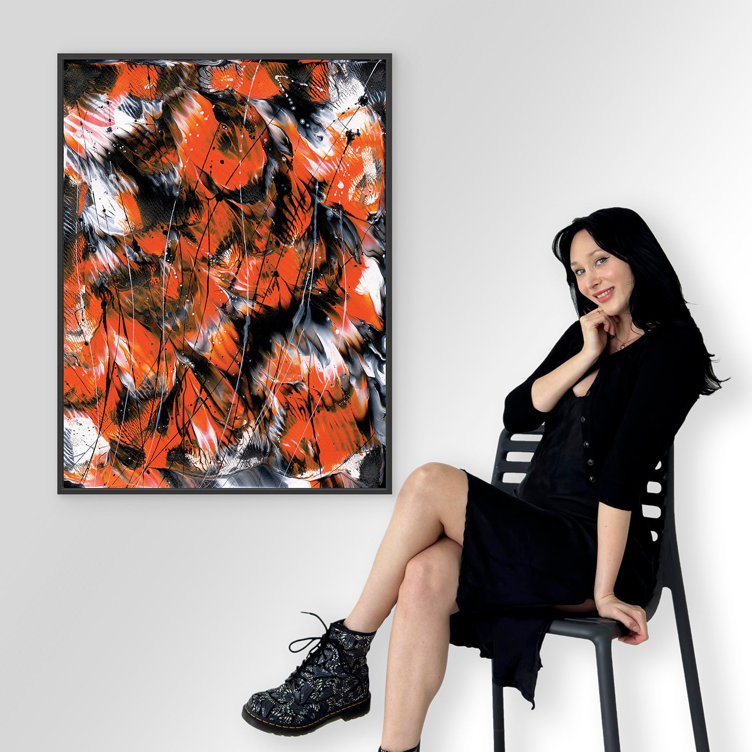 Bridget Bradley sitting on a chair next to a large abstract expressionism fine art print  'Monarch 2' with orange, black, and white colours.