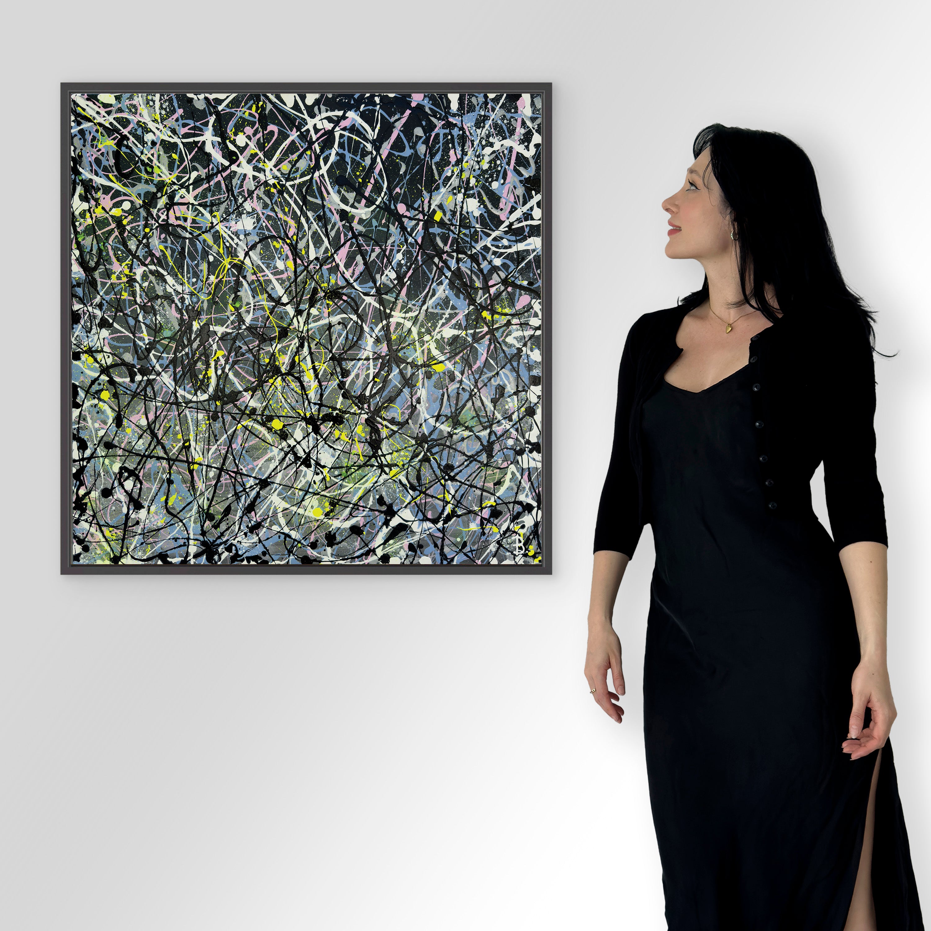 Image of Bridget Bradley abstract expressionist artist dressed in black, standing next to her fine art print,'GREY I' in black float frame hanging on white wall.