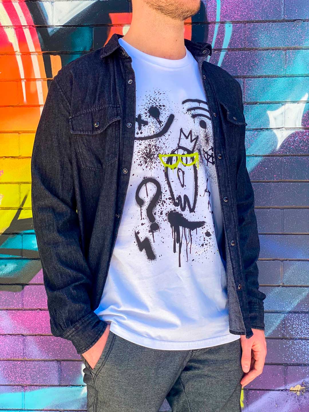 Model wars 'Off Grid' Men's T-Shirt under a denim shirt, standing against a painted wall background. B. Contemporary Streetwear t-shirt print design by Bridget Bradley