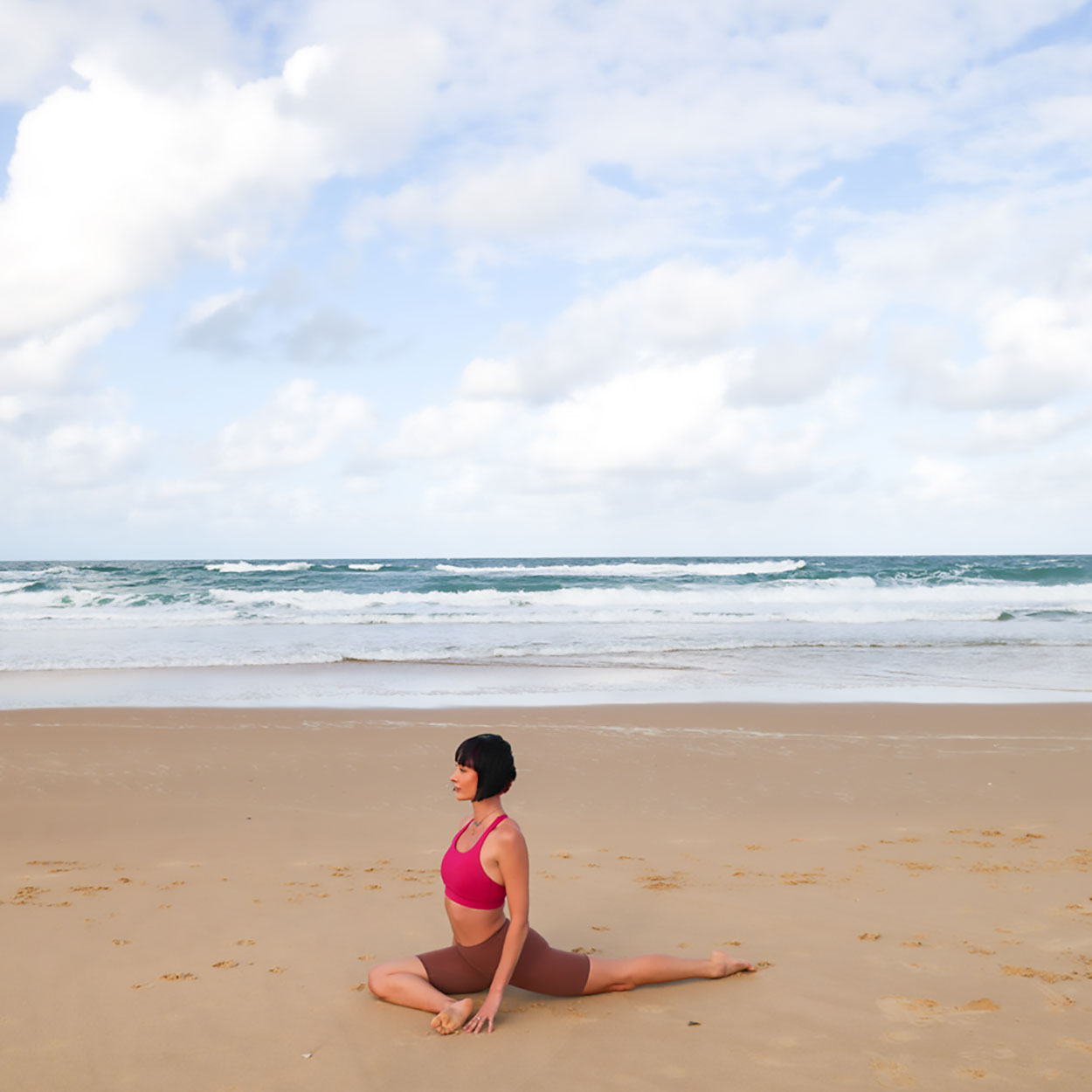 Bridget seen in Pidgeon Pose on sandy beach. B. Yoga by Bridget Bradley
