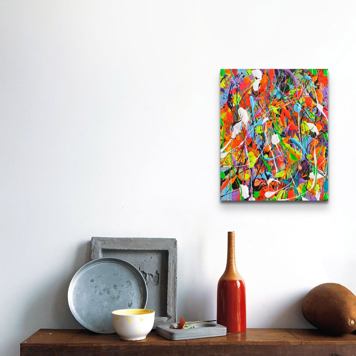 Night at the Carnival, original canvas painting by Bridget Bradley seen in situ above wooden bench with red bottle.