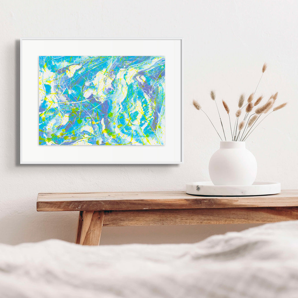 'Atmosphere' original abstratc painting on paper seen hanging in situ with white frame and whote mat above a wooden table with white vase. Colorfyl blues with white and neon yellow. Hand painted by Bridget Bradley, Abstract Artist, Australia