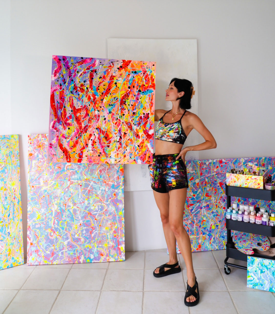 Abstract Artist, Bridget Bradley stands holding her original painting 'Alive' and surrounded by her other abstract artworks and art materials