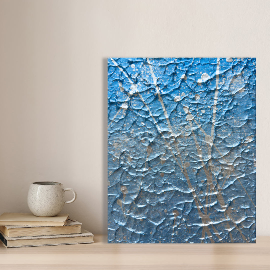 'Ocean Mist' Original Abstract Expressionism Textured Painting in blue and silver palette in Situ near Books with a cup on top. Artwork by Bridget Bradley. Learn more